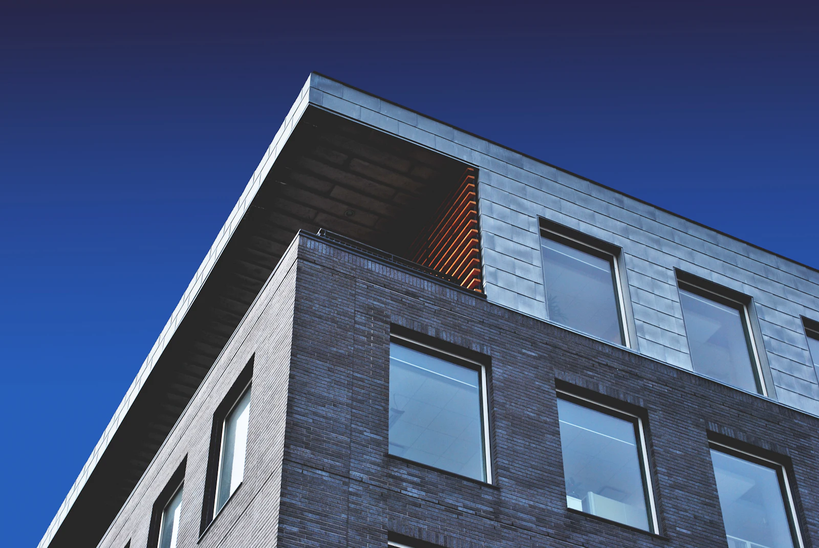The Foundry at dusk — a dark brick cultural building rising into a deep blue sky, warm light held in a carved timber opening